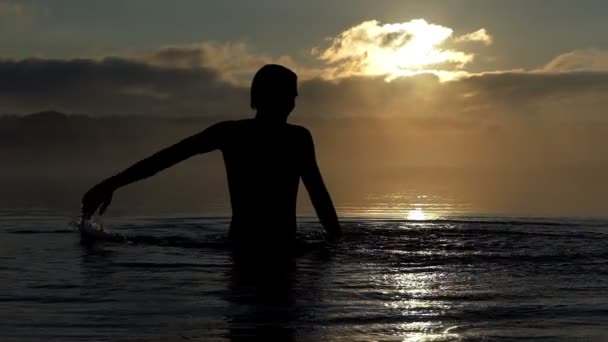 L'uomo felice solleva corsi d'acqua in un lago al tramonto a Slo-mo — Video Stock
