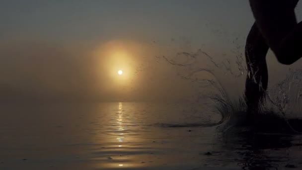 Młody człowiek działa w mgliste jezioro o zachodzie słońca w slo-mo — Wideo stockowe