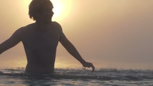 Vrolijke man speelt met meer water in de zomer bij zonsondergang in slo-mo — Stockvideo