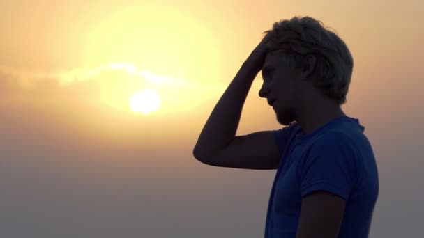 Jonge man zet zijn haar in volgorde bij een prachtige zonsondergang in slo-mo — Stockvideo