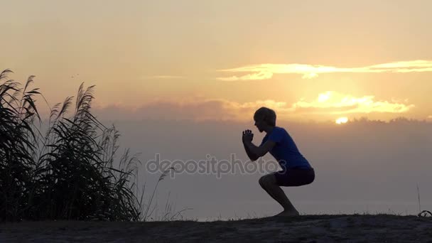 Jovem faz sit-ups em um banco do lago ao pôr do sol em slo-mo — Vídeo de Stock