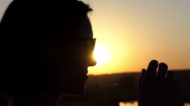 Een jonge slanke vrouw staat en opstijgt naar haar zonnebril bij zonsondergang in Slo-Mo — Stockvideo