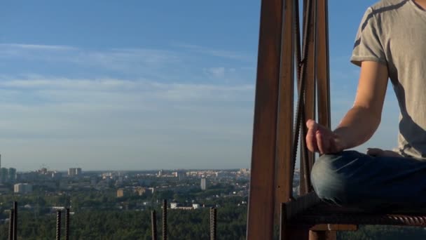 Young man mediatates on a metallic ladder on a house in summer. — Stock Video