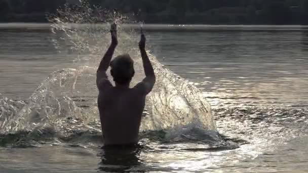 Blonde man werpt stromen van water in een meer bij zonsondergang in slo-mo — Stockvideo