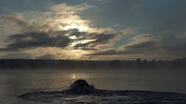 若い男を実行し、スローモーションで夕暮れ時の湖でクロールを泳ぐ — ストック動画