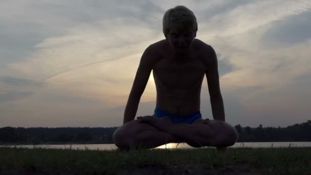 Yogi man sitter i en lotus och höjer sin kropp vid solnedgången i slo-mo — Stockvideo