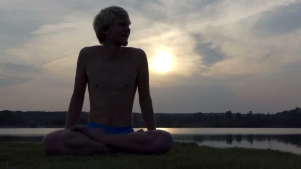 Yogi uomo siede in un loto e solleva il suo corpo al tramonto in slo-mo — Video Stock