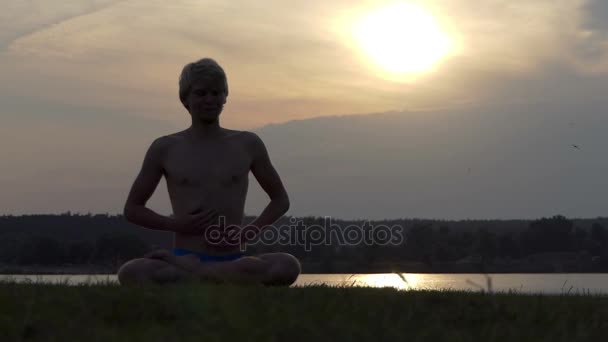 Yogi ül a Lotus, tartja a kezét a mellkasára, napnyugtakor a slo-mo — Stock videók