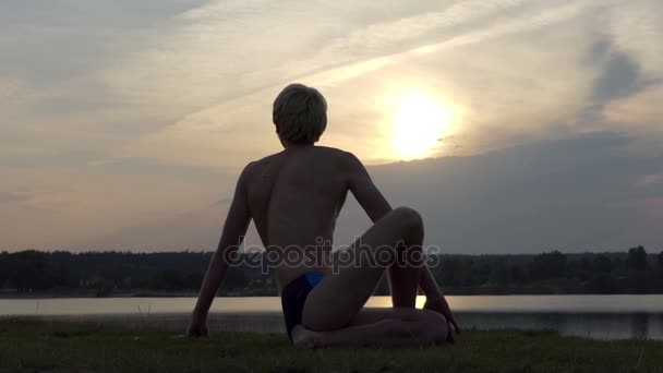 Feliz yogui se sienta en una posición de águila en una orilla del lago en slo-mo — Vídeos de Stock