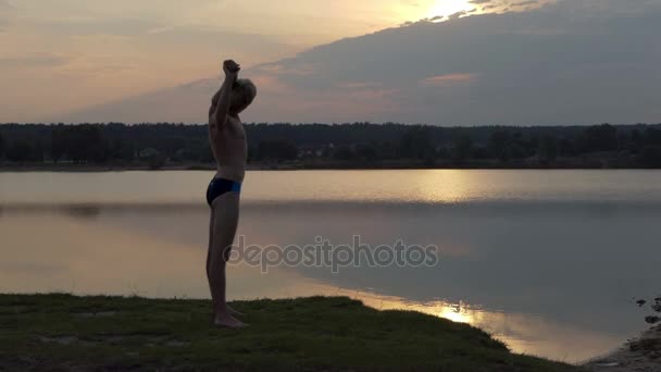Молодий чоловік розтягує плечі на березі озера в шлю-мо — стокове відео