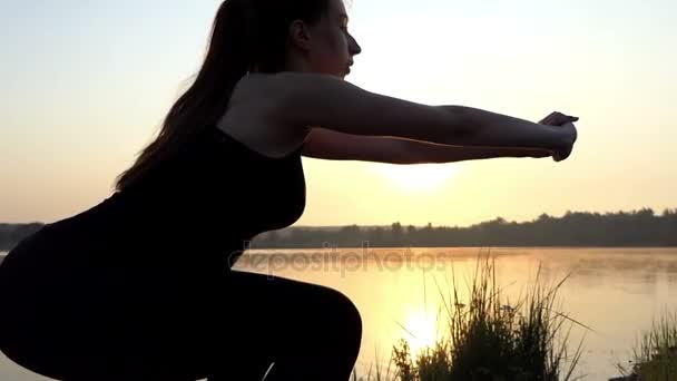 Dwie dziewczyny zrobić squats o zachodzie słońca w pobliżu jeziora. — Wideo stockowe