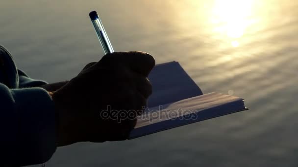 Mujer pone en su bloc de notas en una orilla del lago al atardecer en slo-mo — Vídeos de Stock