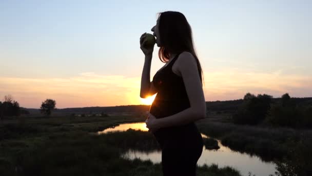 Vacker gravid kvinna äta grönt äpple i solnedgången. — Stockvideo