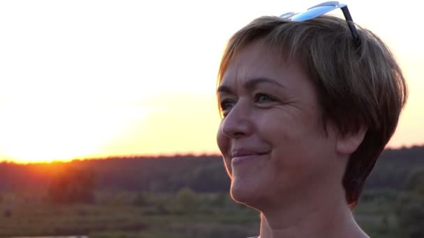 Vackra medelålders kvinna som tittar någonstans vid solnedgången. — Stockvideo