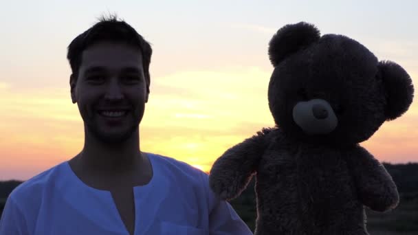 Lustige Mann spielen mit großen Bären Spielzeug bei Sonnenuntergang. — Stockvideo