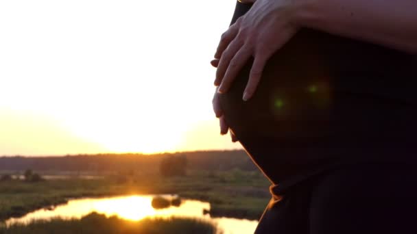 Hände des Mädchens berühren ihren schwangeren Bauch bei Sonnenuntergang in Zeitlupe. — Stockvideo