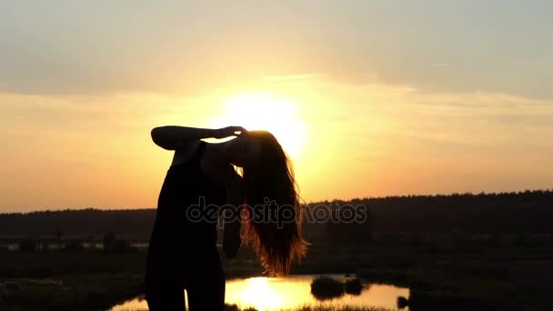 La silueta de la joven juega con sus pelos al atardecer . — Vídeos de Stock