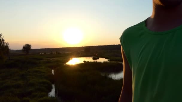 Glimlachende man in groen t-shirt kleden zonnebril bij zonsondergang in slow motion. — Stockvideo