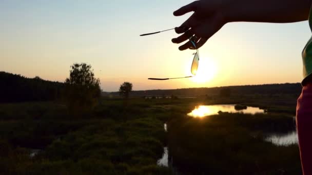 Solglasögon hängande på fingret vid solnedgången i slow motion. — Stockvideo