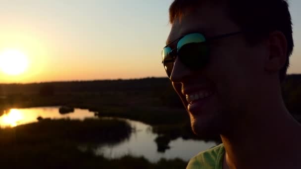 Gün batımında güneş gözlüklü genç adam gülümseyen bir siluet. — Stok video