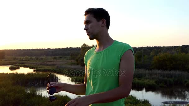 Jeune homme habille les lunettes de soleil au coucher du soleil au ralenti . — Video