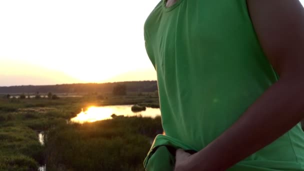 Mann im grünen T-Shirt saubere Sonnenbrille bei Sonnenuntergang. — Stockvideo