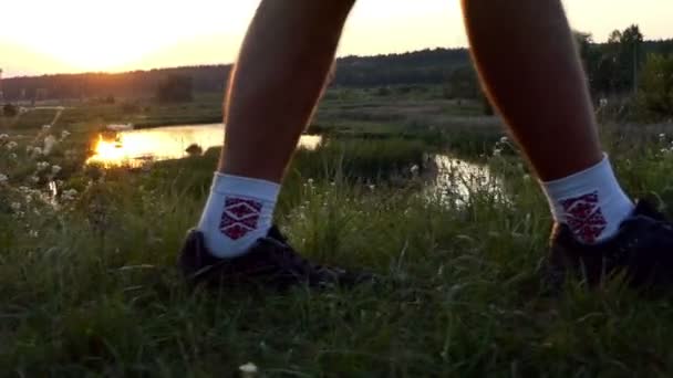 Man in folk sokken lopen op het gras bij zonsondergang. — Stockvideo