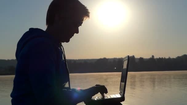 Uma mulher de meia-idade imprime num portátil ao pôr-do-sol — Vídeo de Stock
