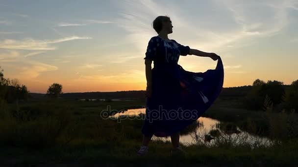 Medelålders kvinna i en folk klänning står vid solnedgången — Stockvideo