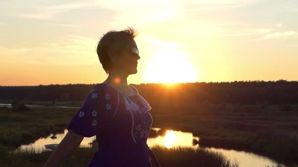 Vrolijke vrouw golven de zoom van haar jurk bij zonsondergang — Stockvideo