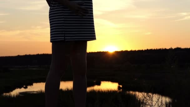 Jovem grávida fica em um banco do lago ao pôr do sol em slo-mo — Vídeo de Stock