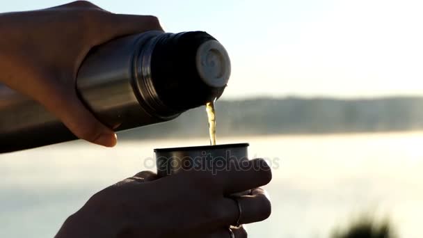 Hett vatten hälls i en kolv kopp på en sjön bank vid solnedgången — Stockvideo