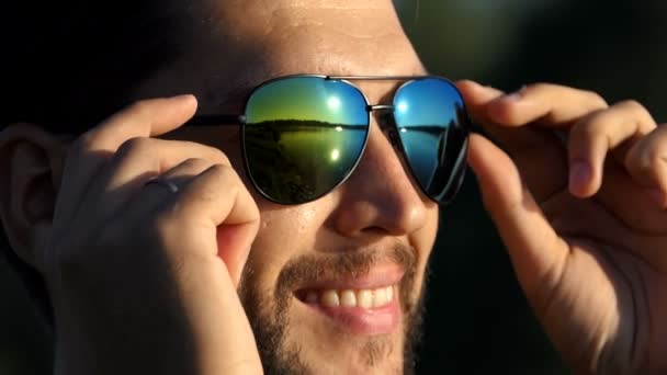 El hombre se quita las gafas de sol en una orilla del lago y sonríe en slo-mo — Vídeo de stock