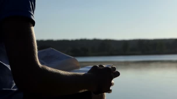 Jovem olha para fotos de família em um banco de lago no verão — Vídeo de Stock