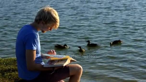 Un homme intelligent regarde des photos. Les canards nagent à proximité dans un lac — Video