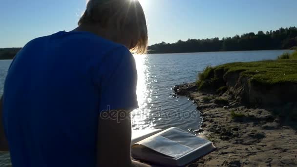 L'homme est assis en semi-profil et regarde des photos sur une rive de lac — Video