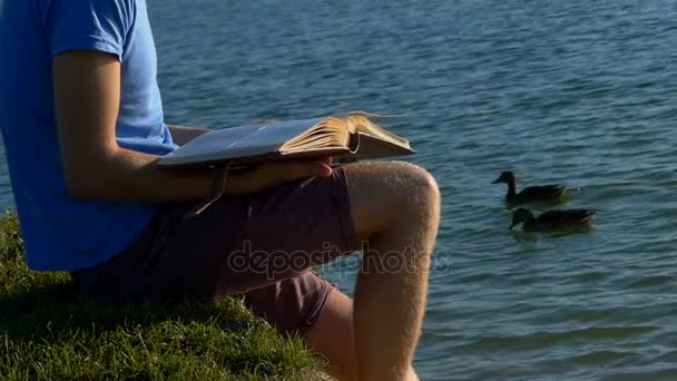 Genç adam bir göl kıyısında fotoğraf bakar. Kahverengi ördek yüzmek yakın — Stok video