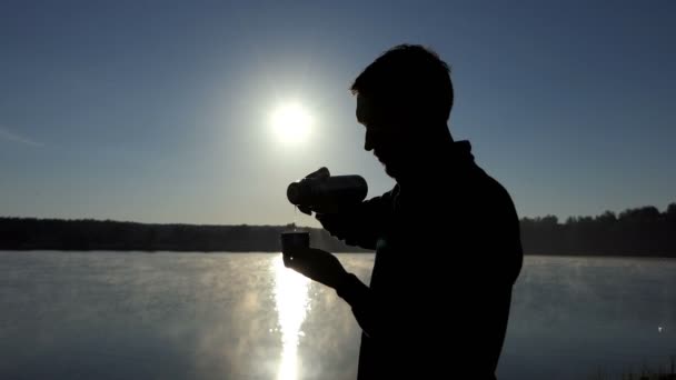 Молодой человек наливает горячий чай из фляжки в чашку на закате в 4k — стоковое видео