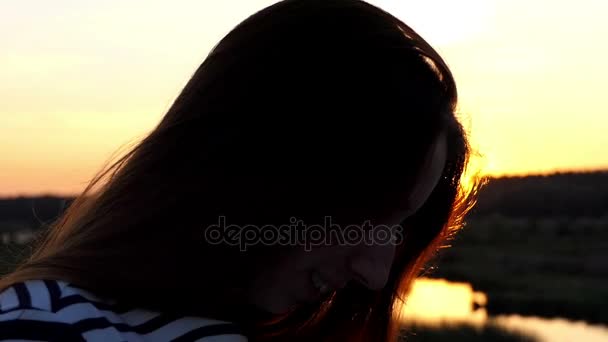 Mulher grávida bonita em um vestido listrado está em um banco do lago ao pôr do sol — Vídeo de Stock