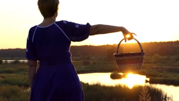 Mujer feliz gira una cesta popular en una orilla del lago al atardecer en slo-mo — Vídeo de stock