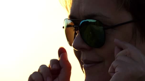 Жінка знімає сонцезахисні окуляри і посміхається на заході сонця в шлю-мо — стокове відео