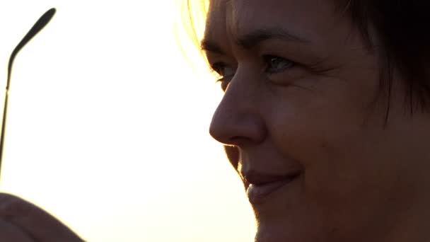 Smiling woman puts on her sunglasses on a lake bank at susnet — Stock Video