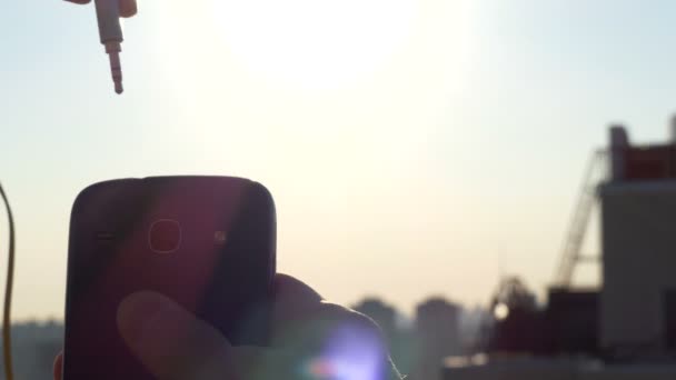 4k - 3,5 mm hoofdtelefoon invoegen in de telefoon bij zonsondergang. — Stockvideo