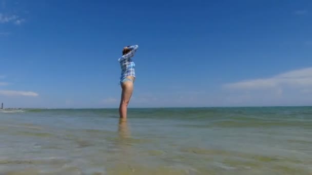 Een jonge vrouw in een geruit overhemd staat in de zee — Stockvideo