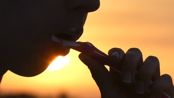 Jovem mulher limpa os dentes com uma escova de plástico ao pôr do sol — Vídeo de Stock