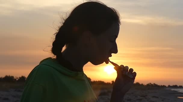 Hermosa mujer limpia sus dientes con un cepillo de plástico al atardecer — Vídeo de stock