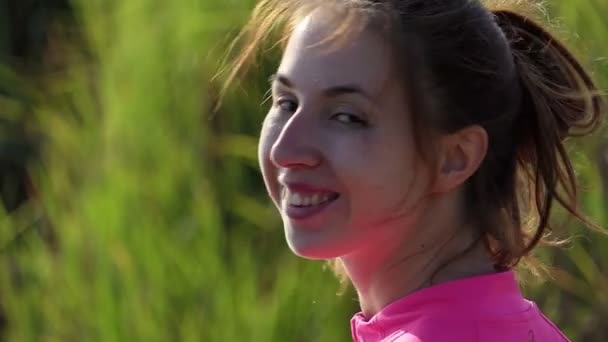 Χαμογελώντας νεαρή γυναίκα σε μια τράπεζα στη λίμνη το καλοκαίρι σε slo-mo — Αρχείο Βίντεο