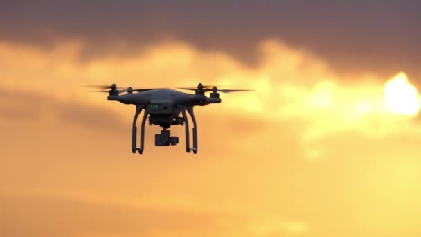 Een vliegende quadracopter met vier roterende bladen bij zonsondergang in slo-mo — Stockvideo