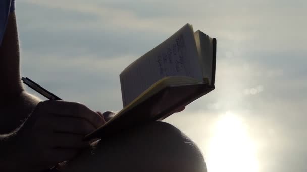 El hombre creativo se sienta en una orilla del lago y escribe algo en slo-mo — Vídeo de stock