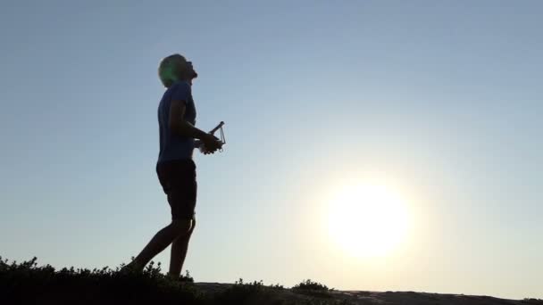 Young man operstes a flying drone with his panel at sunset in slo-mo — Stock Video